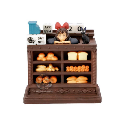 Calendario perpetuo ufficiale Studio Ghibli ispirato a Kiki - Consegne a domicilio, con Kiki in grembiule dietro il bancone del pane insieme al gatto Jiji e dadi per la data