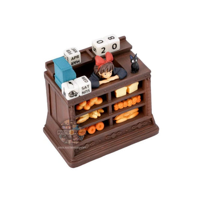 Calendario perpetuo ufficiale Studio Ghibli ispirato a Kiki - Consegne a domicilio, con Kiki in grembiule dietro il bancone del pane insieme al gatto Jiji e dadi per la data